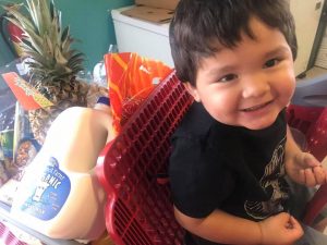 A child sitting in a Storehouse shopping cart full of fresh food. It is extremely important to us to feed children living in food deserts.