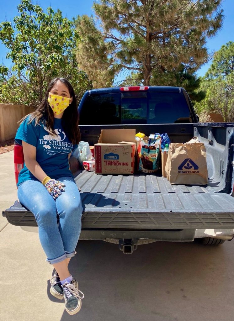 Izzy sits on a truck with some of her Grub Crawl food donations. She is wearing a mask and gloves due to Coronavirus, and is smiling for the camera. 