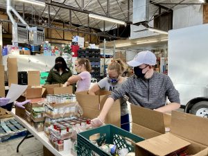 volunteers needed at the Storehouse, teens packing boxes of food for families in need
