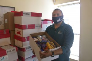 Staff Member Tim holds a box of food for a family. He is wearing a mask.