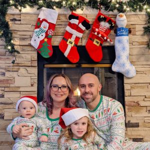 A picture of the Trujillo family with their two children. They sit in front of a fireplace with stockings hanging.