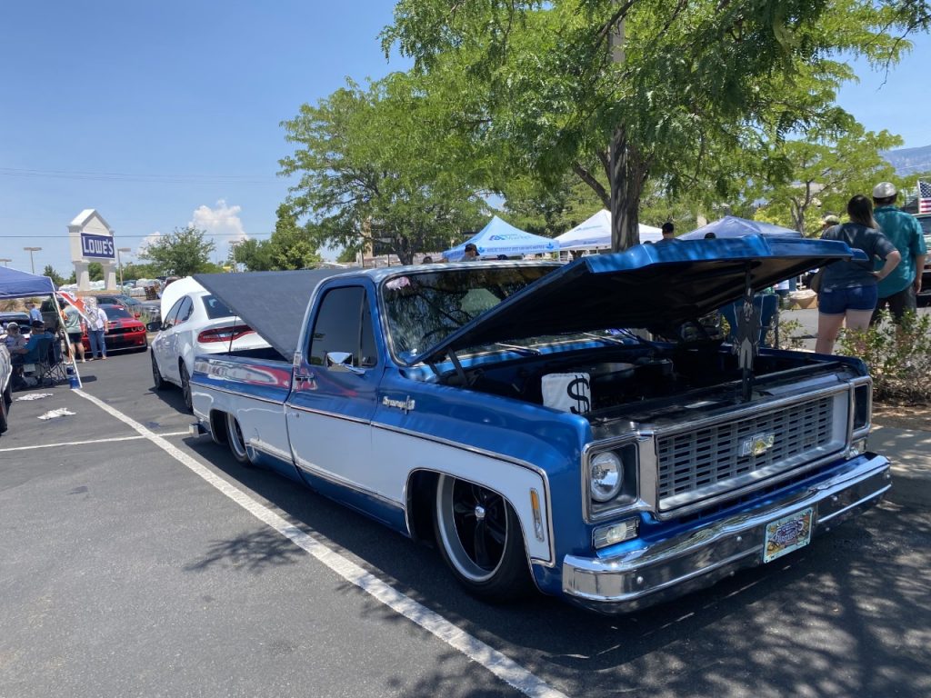a blue and white truck participated in Hot Rods for Hunger in 2021 is pictured with cars and people behind it. 