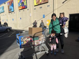 A mother and two young children with a grocery cart full of food outside of the Storehouse.